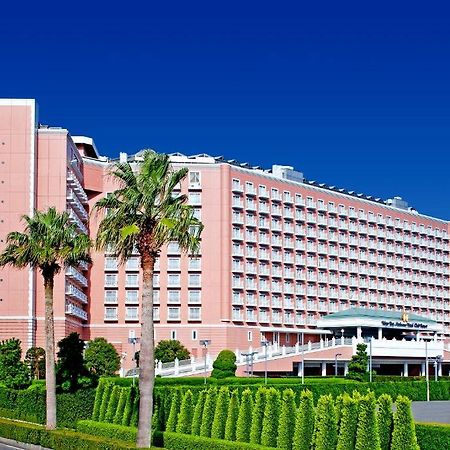 Hotel Grand Nikko Tokyo Bay Maihama Urayasu Exterior foto The image shows a large, multi-story hotel building featuring a light pink facade. The architecture appears modern, with numerous windows arranged in a grid pattern. In the foreground, there are neatly trimmed shrubs and palm trees, adding a tropical