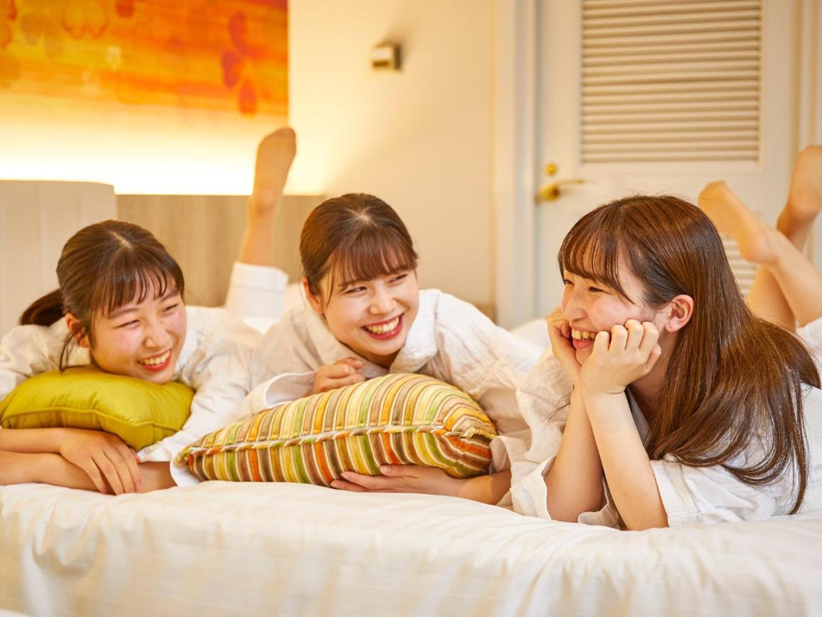 Hotel Grand Nikko Tokyo Bay Maihama Urayasu Exterior foto The photo shows three young women lounging together in a cozy indoor setting. They are dressed in white robes and appear to be relaxed and enjoying each other's company. The women are lying on a bed, with two of them resting on their arms and the thi