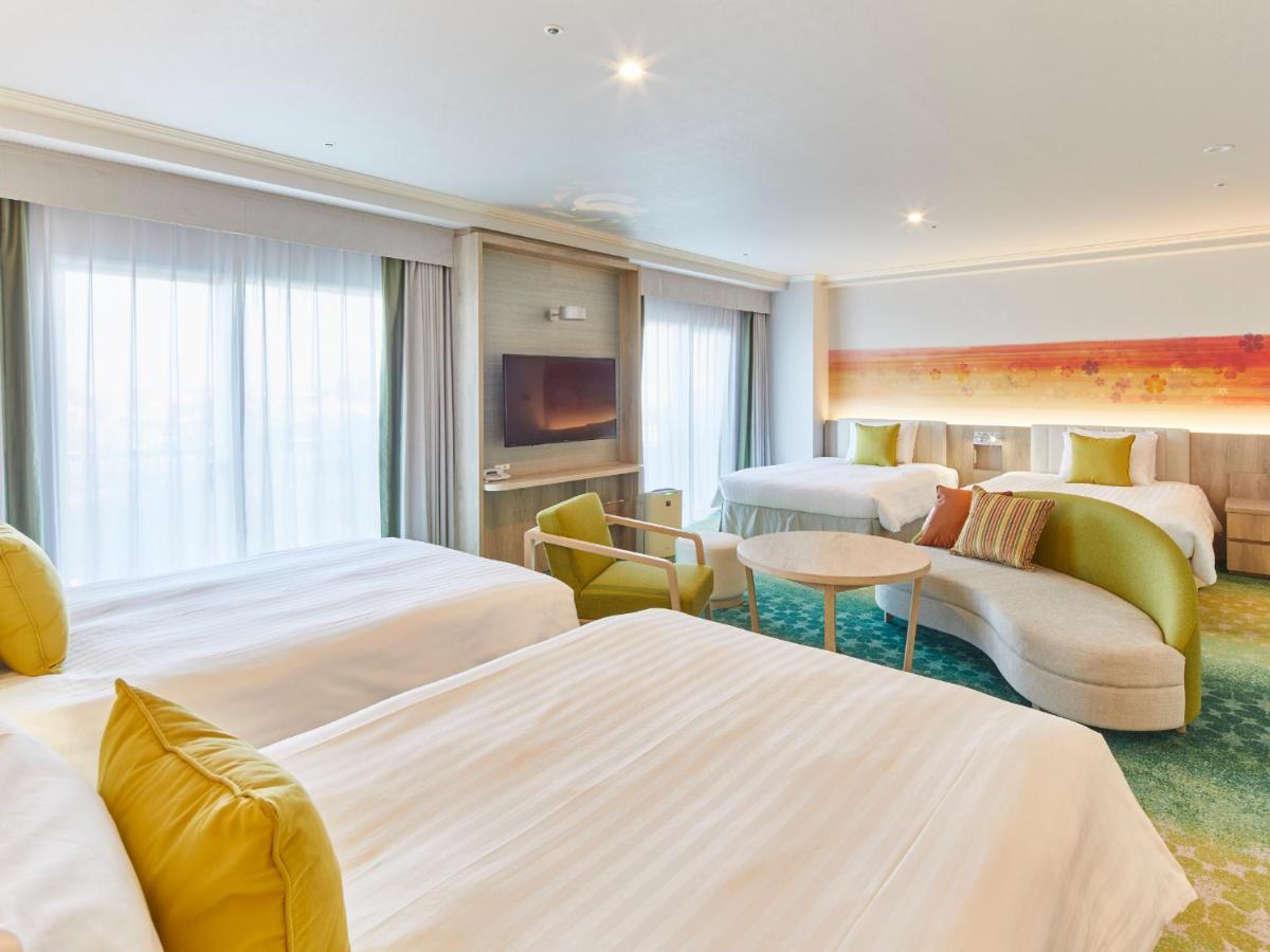 Hotel Grand Nikko Tokyo Bay Maihama Urayasu Exterior foto The photo shows a modern hotel room that features two large beds covered with white bedding and decorative pillows. There is a contemporary, curved sofa in a light color, along with a round table in the middle. The room has large windows that allow n