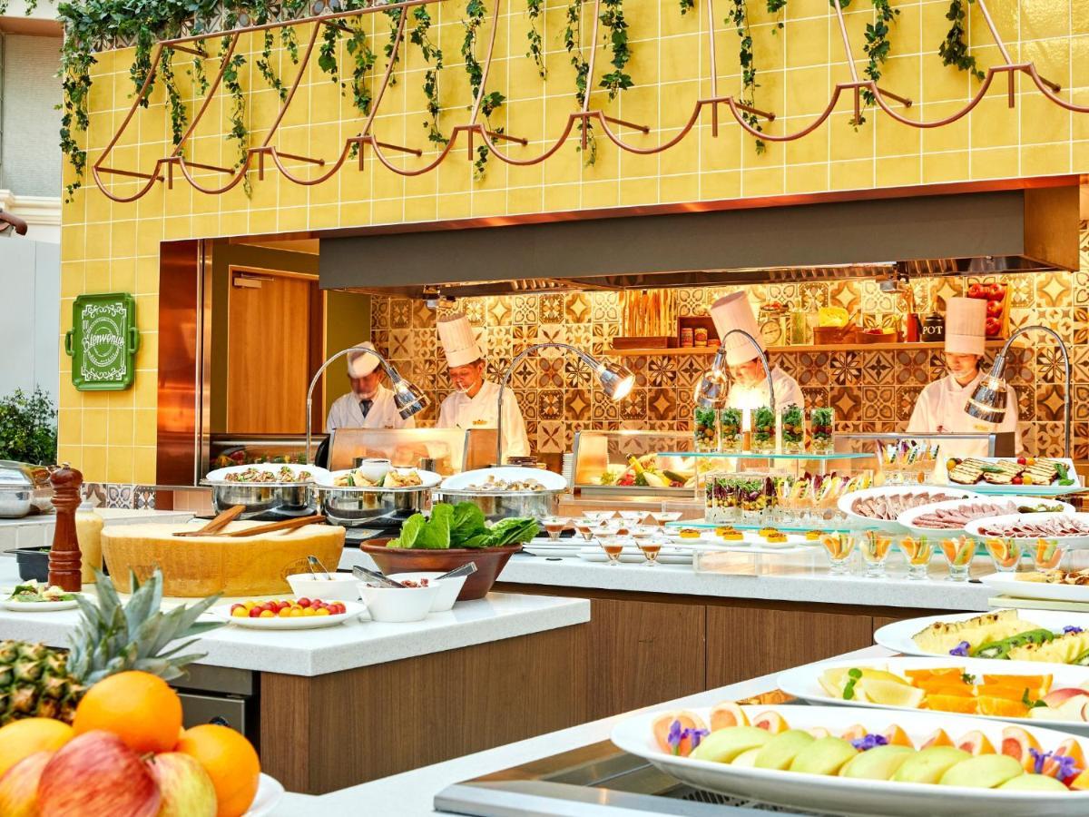 Hotel Grand Nikko Tokyo Bay Maihama Urayasu Exterior foto The photo shows a vibrant and colorful buffet setup in a restaurant. In the foreground, there are various dishes arranged on white platters, featuring an assortment of fruits, desserts, and other items. The background features chefs in white uniforms