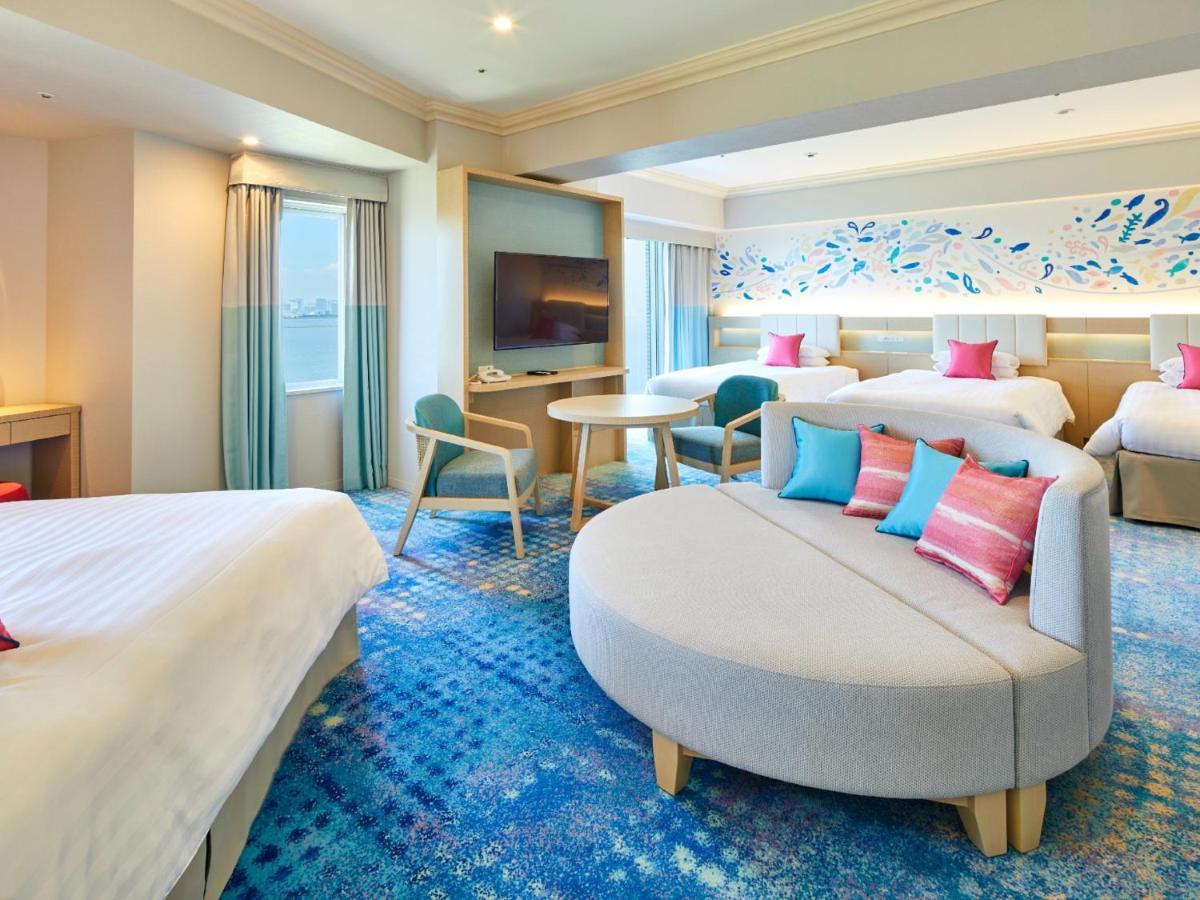 Hotel Grand Nikko Tokyo Bay Maihama Urayasu Exterior foto The photo shows a modern hotel room featuring a spacious layout with multiple beds. There is a large, curved sofa with colorful cushions in the center, adding a contemporary touch to the design. The room has large windows allowing natural light to fi