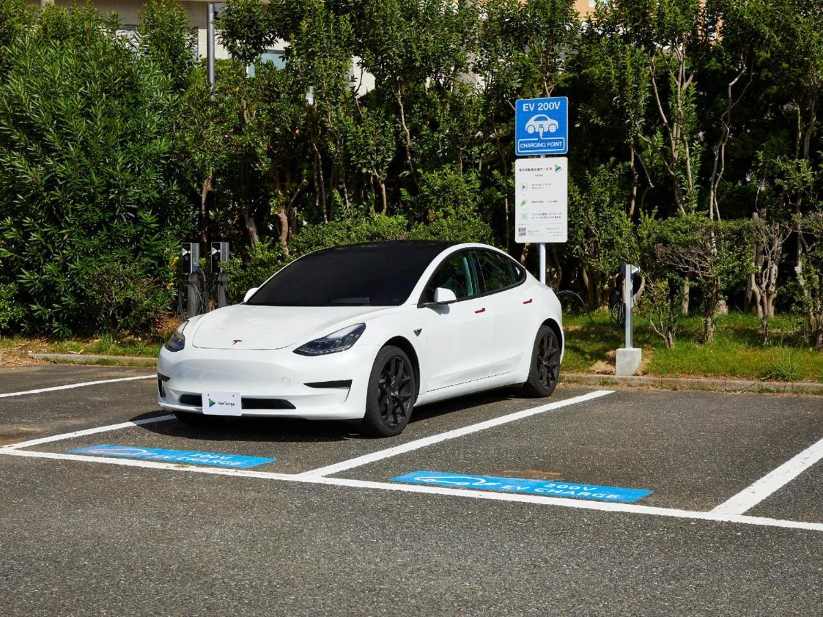 Hotel Grand Nikko Tokyo Bay Maihama Urayasu Exterior foto The photo shows a white electric car parked in an EV (electric vehicle) charging spot. The car has a sleek design with black wheels and tinted windows. In the background, there are green shrubs and trees, indicating a natural or landscaped environmen