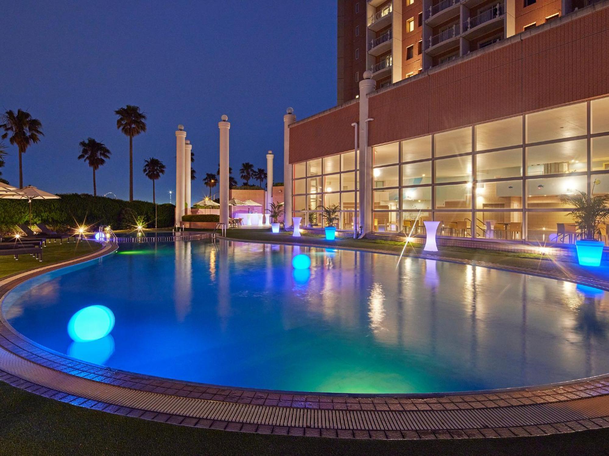 Hotel Grand Nikko Tokyo Bay Maihama Urayasu Exterior foto The photo shows a well-lit swimming pool at night, surrounded by a lush green area. The pool features glowing blue lights that create a serene and inviting atmosphere. Palm trees can be seen in the background, adding a tropical feel to the scene. Add
