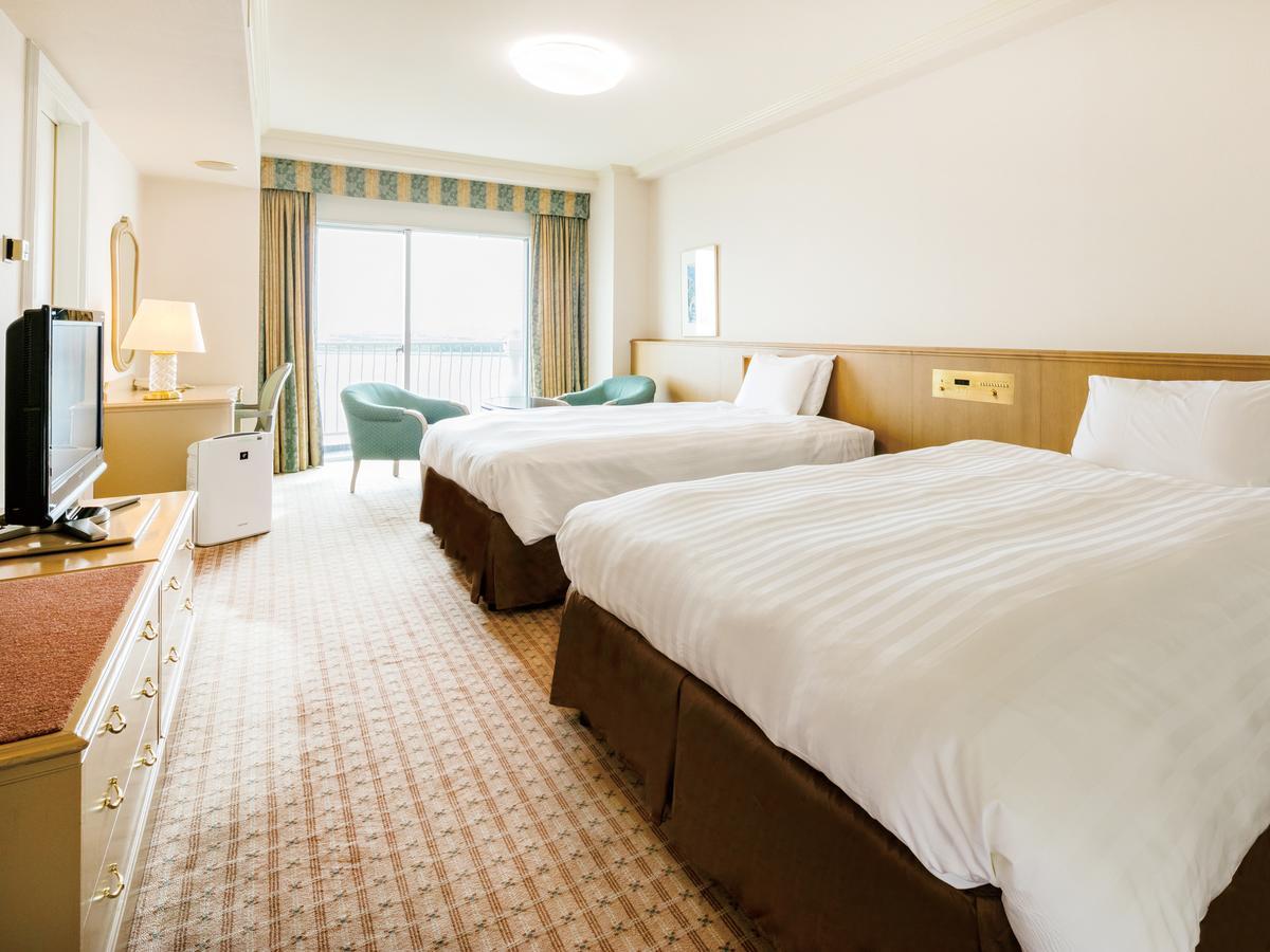 Hotel Grand Nikko Tokyo Bay Maihama Urayasu Exterior foto The photo shows a hotel room featuring two large beds with white bedding and brown bases. There's a light-colored carpet on the floor, and the room is brightly lit. To one side, there is a television on a stand and a small white refrigerator. A desk 